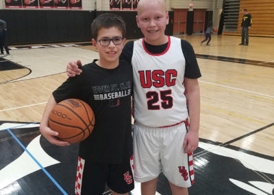 two young boys standing next to each other on a basketball court