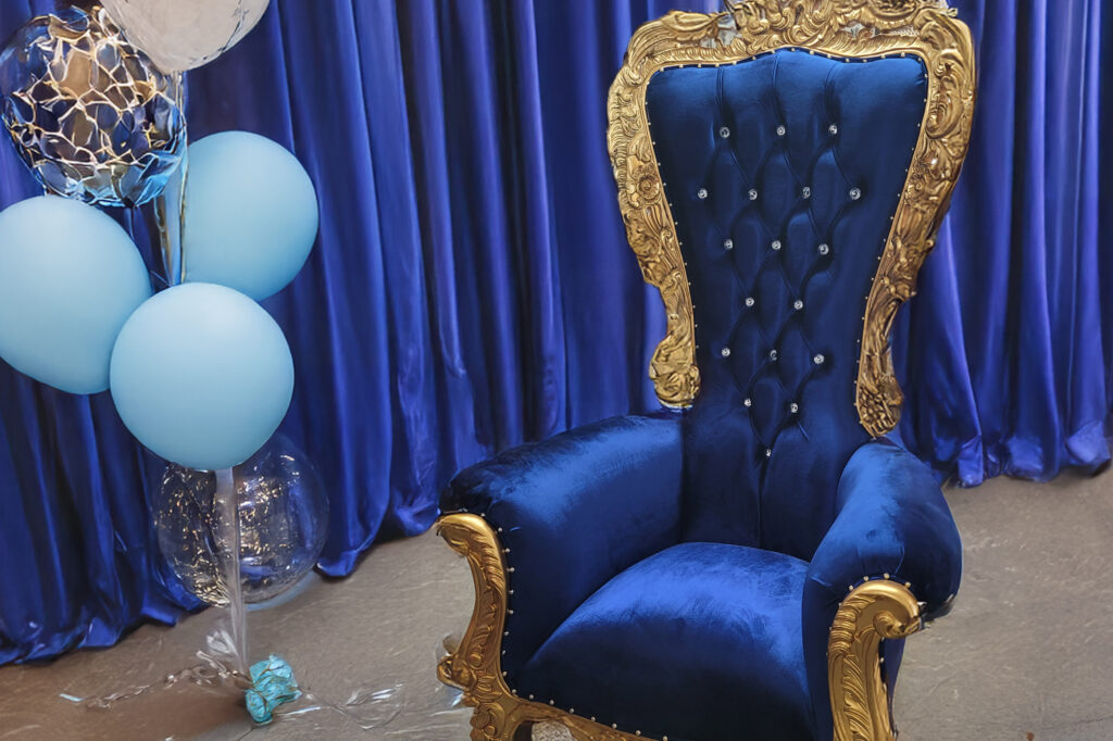 a blue and gold chair and balloons in front of a blue curtain
